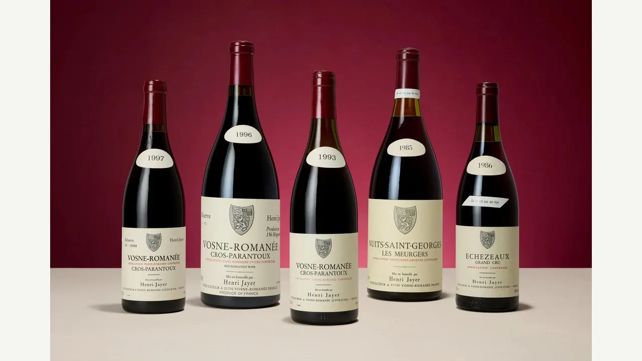 Cinque bottiglie di Borgogna di Henri Jayer (Vosne-Romanée Cros-Parantoux 1997, 1996, 1993, Nuits-Saint-Georges Les Meurgers 1985, Echezeaux Grand Cru 1986) allineate su sfondo rosso